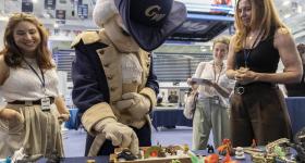 George (mascot) tries out the sand tray at a booth manned by play therapy specialists, including graduate student Haley Giles (left) and Clinical Assistant Professor of Counseling and Human Development Mary DeRaedt (right). 
